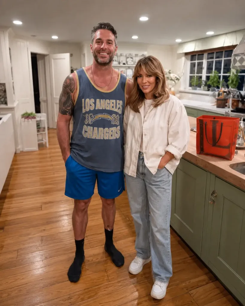 A stylish couple standing in a warm kitchen with sage green cabinets and farmhouse details.